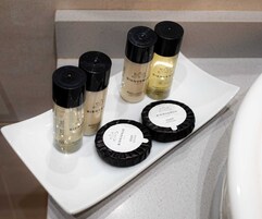Una bandeja rectangular blanca con diversos artículos de aseo, como loción corporal, champú y jabón, sobre una encimera de baño.