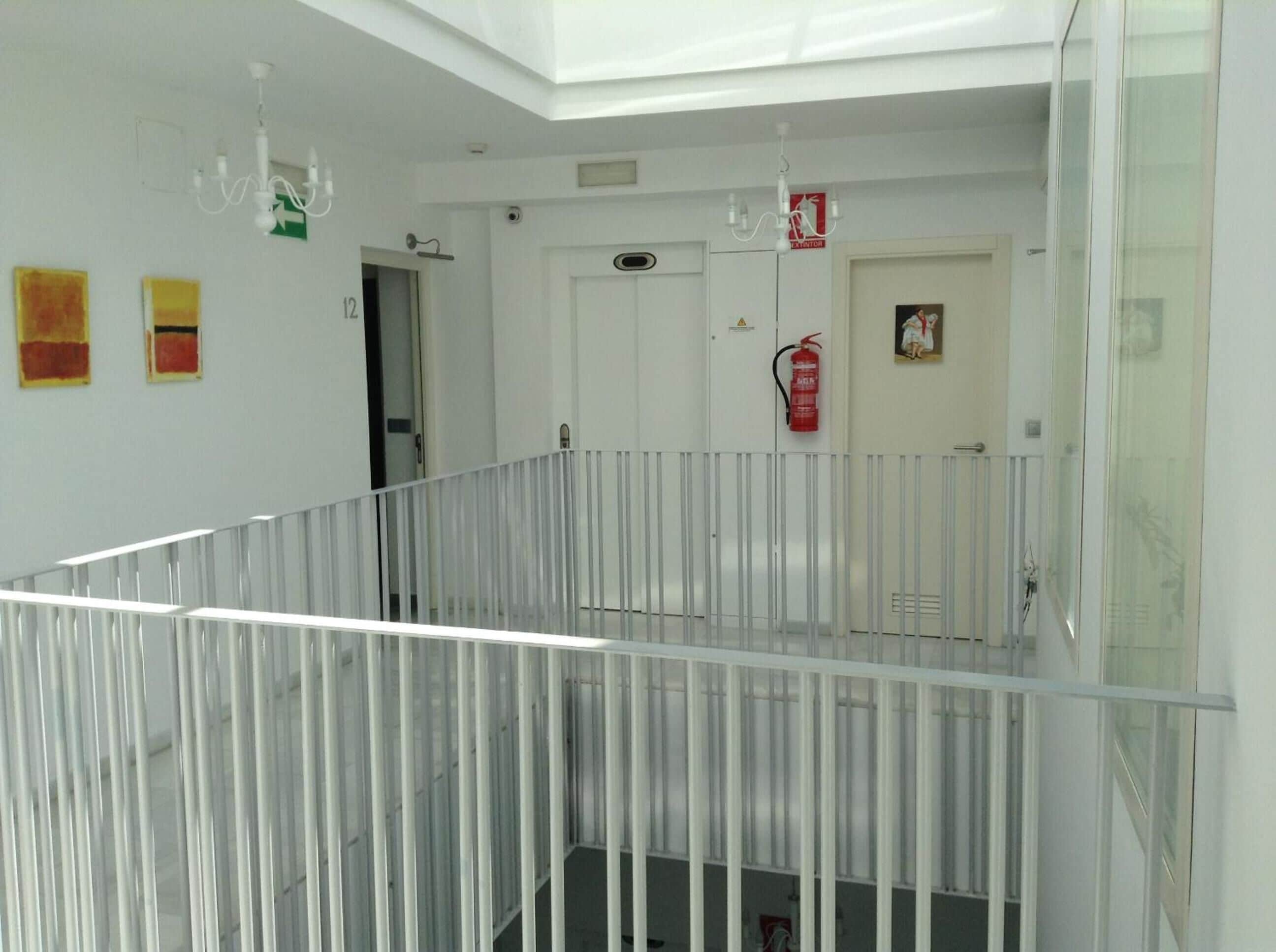Un interior moderno con barandilla de vidrio, paredes blancas y un extintor de incendios montado en la pared.