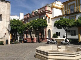 Una plaza histórica con una fuente, rodeada de edificios tradicionales, incluido un hotel.