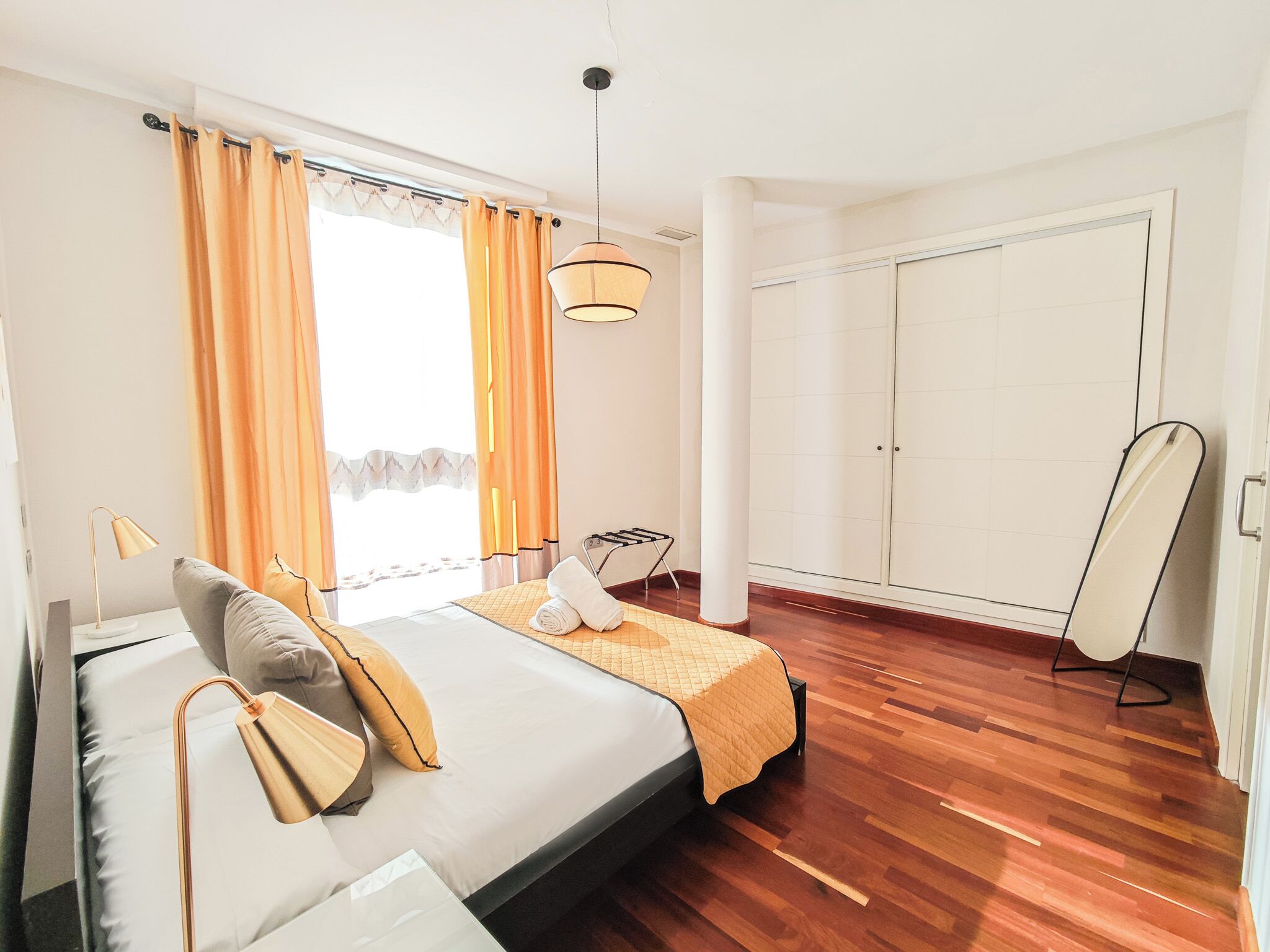 A modern bedroom with a bed, a standing lamp, a wardrobe, and a view of the outdoors.