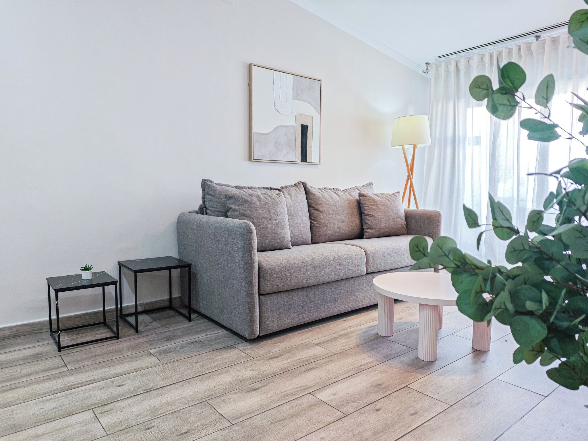 Ein modernes Wohnzimmer mit grauem Sofa, einem kleinen Beistelltisch, einer Stehlampe und einem runden Couchtisch.