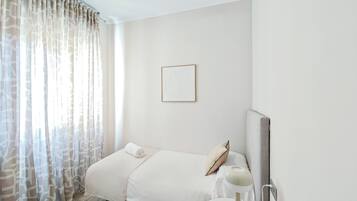 Una habitación de hotel con cama, mesita de noche, un cuadro en la pared y una ventana con cortinas.