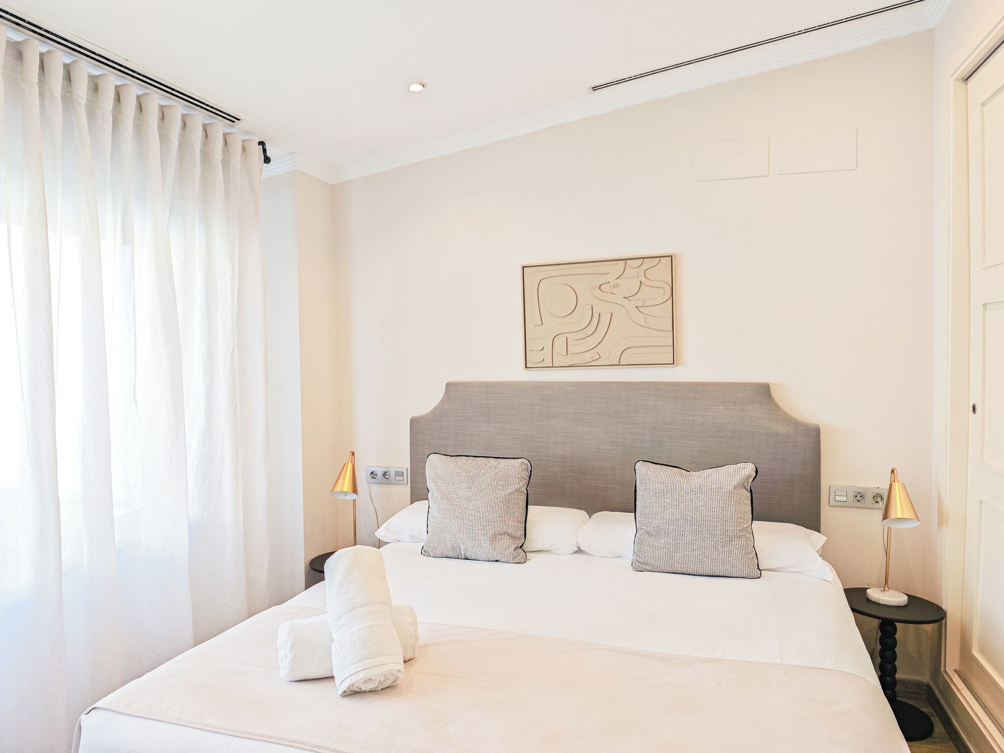 A hotel room with a large bed, two bedside lamps, a headboard with a geometric design, and a wall-mounted artwork.