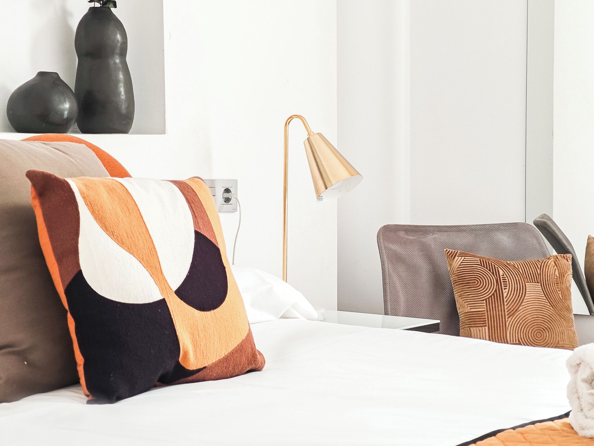 A modern hotel room with a bed, a desk, a lamp, and two vases on the wall.