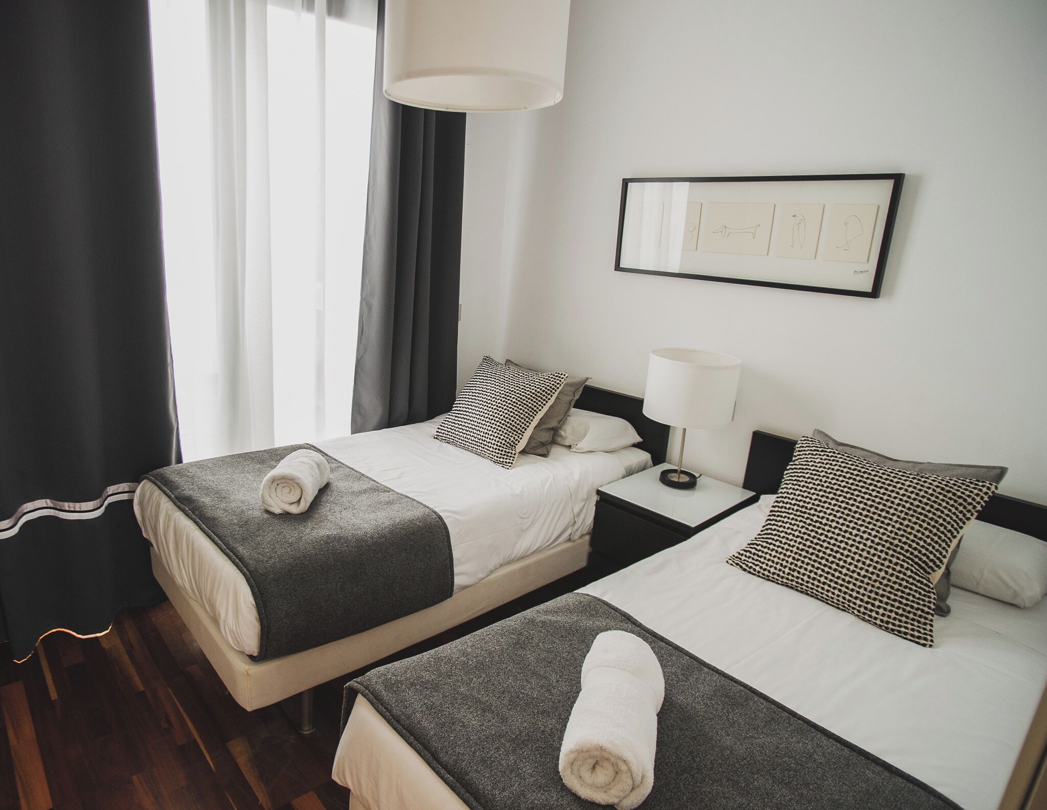Habitació d'hotel amb dos llits, una nit de nit amb una làmpada, un quadre amb marc a la paret i una finestra amb cortines.