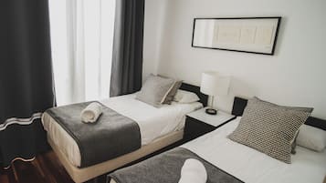 Habitació d'hotel amb dos llits, una nit de nit amb una làmpada, un quadre amb marc a la paret i una finestra amb cortines.