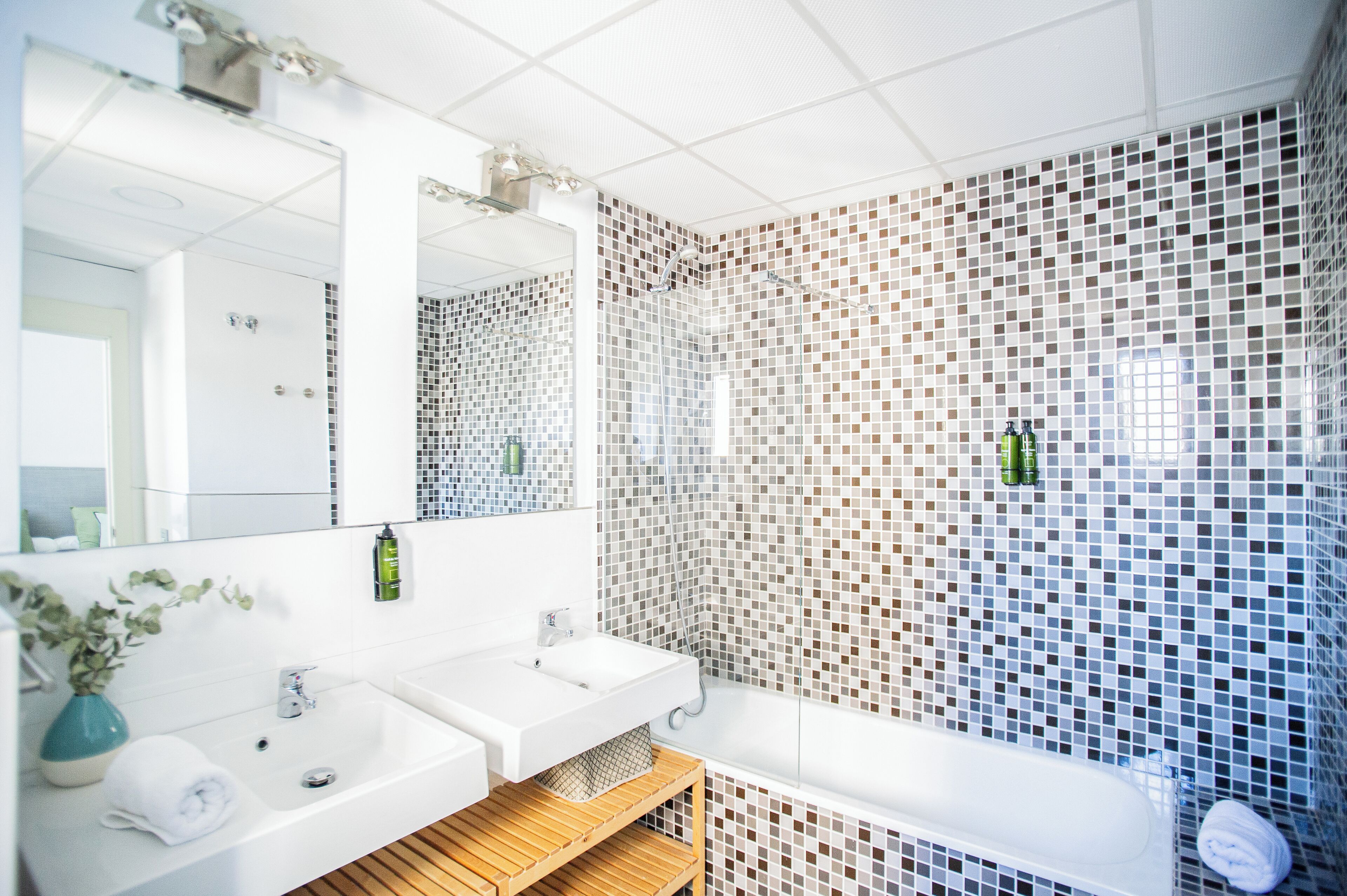 A modern bathroom with two sinks, a large mirror, and a shower area with mosaic tiles.