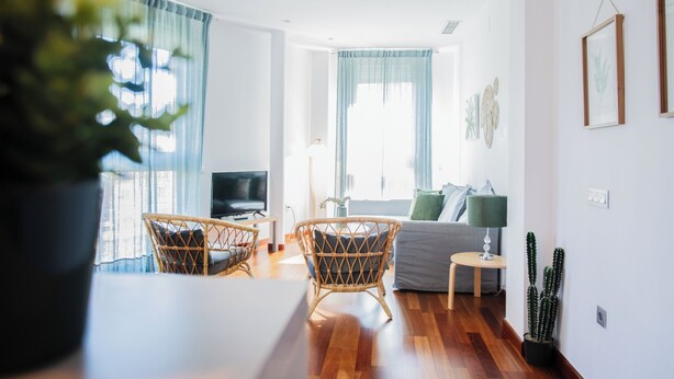 A modern living room with a sofa, two wicker chairs, a small table, and a TV. - AZZ Sevilla Torre de la Plata (Seville)