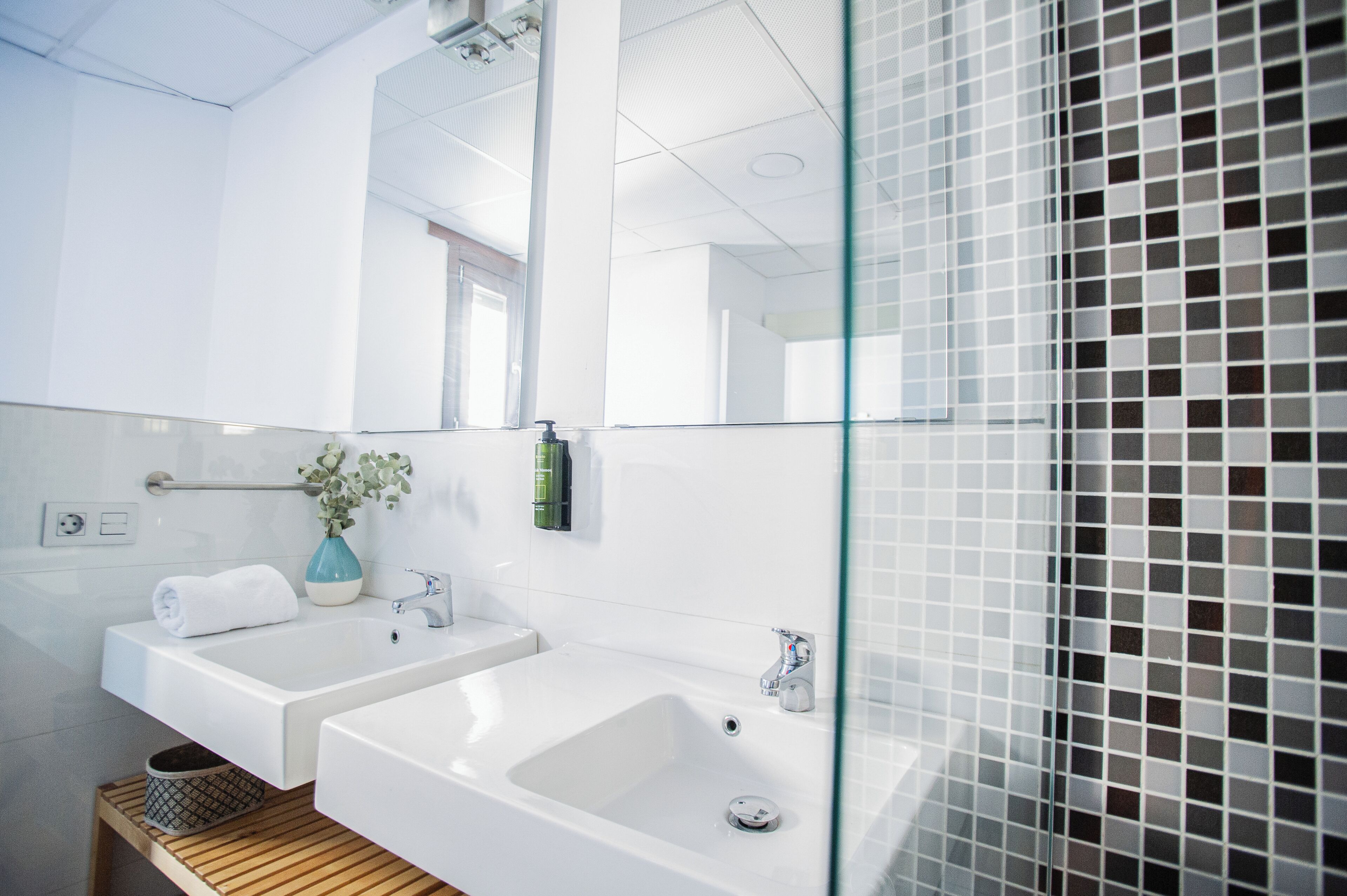 Een moderne badkamer met twee wastafels, een spiegel en een douchecabine met glazen wanden.