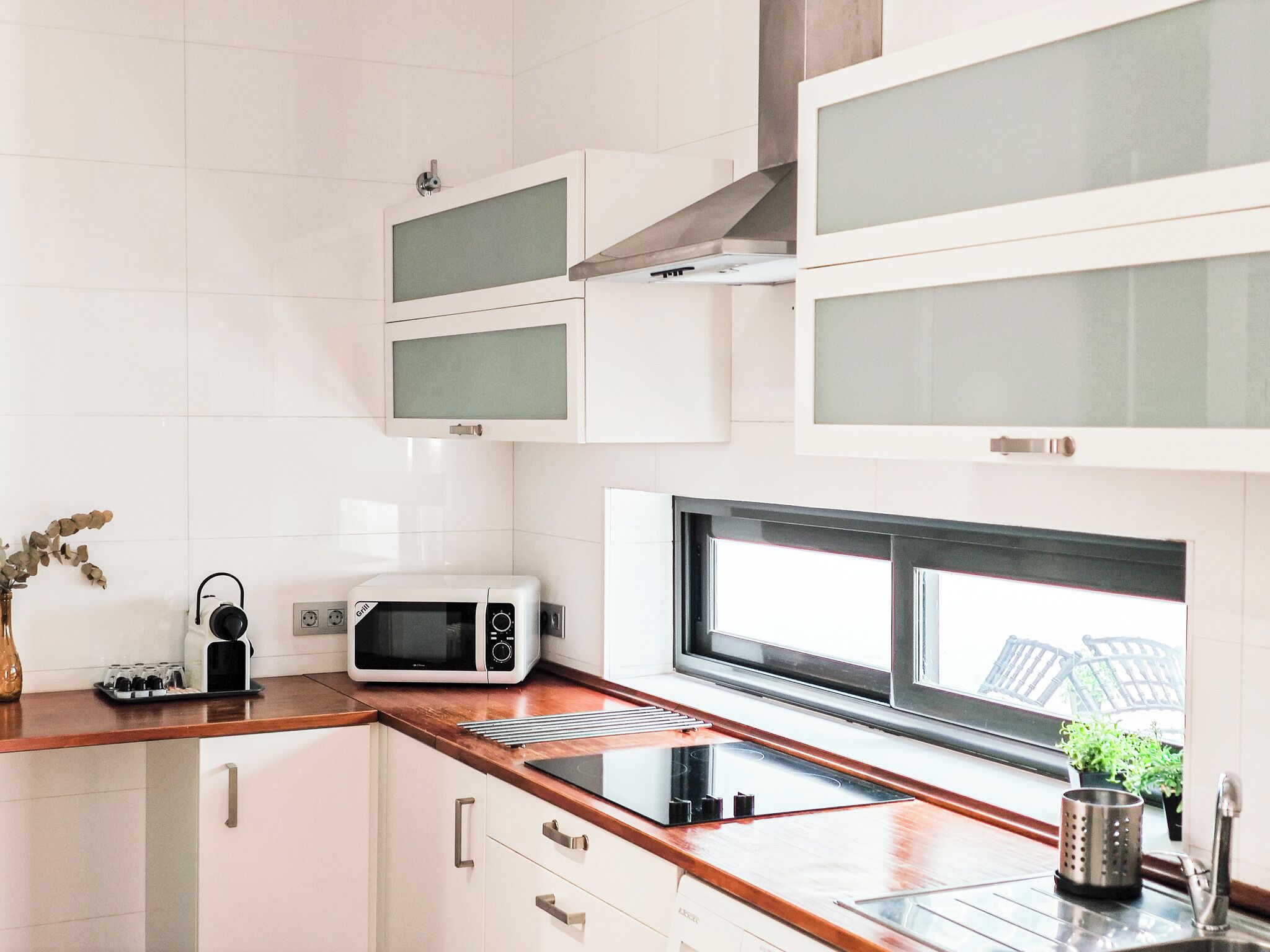A modern kitchen with white cabinets, a microwave, a toaster, and a window above the sink.