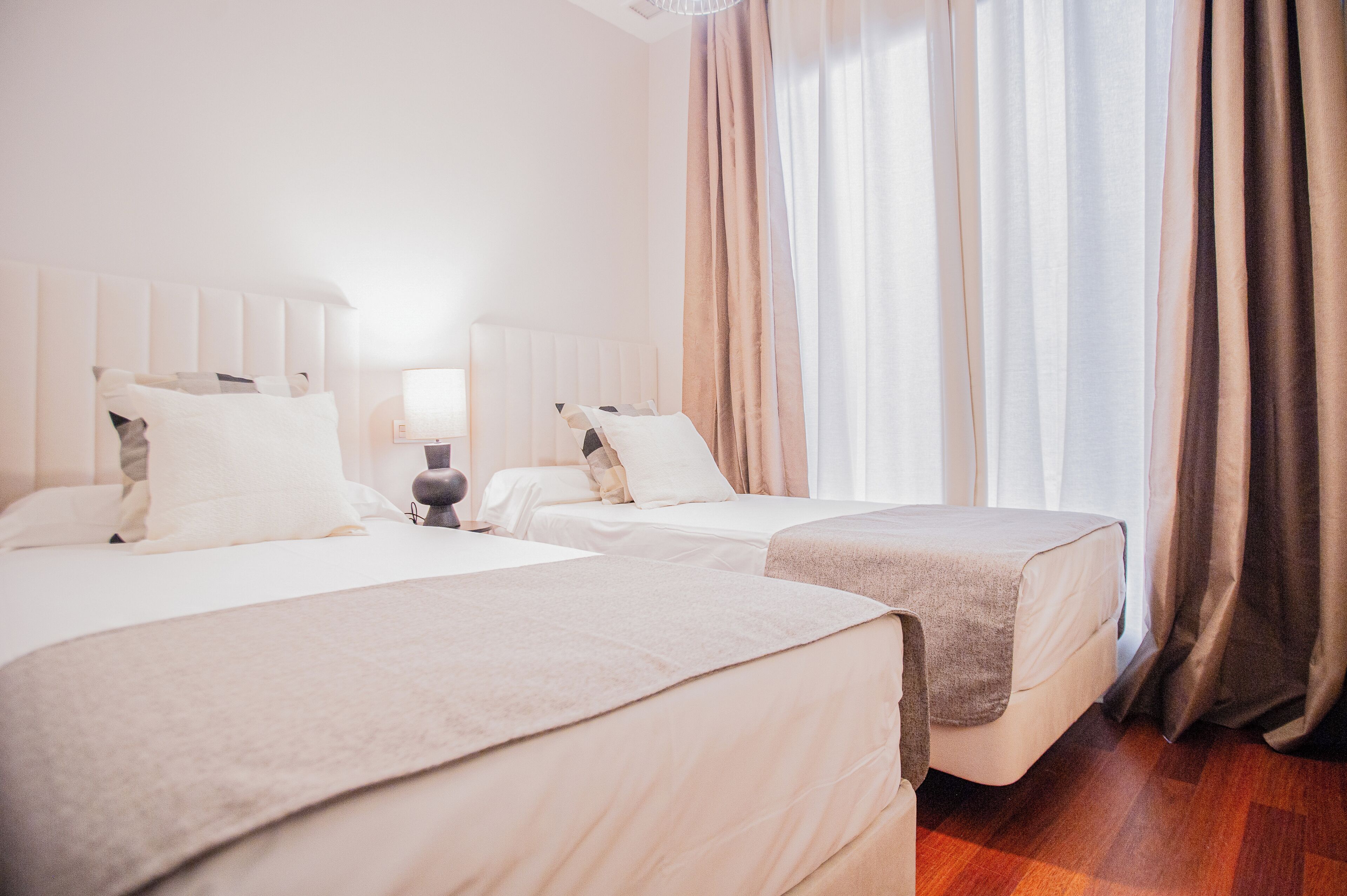 Ein Hotelzimmer mit zwei Betten, einem Nachttisch und einem Fenster mit Vorhängen.