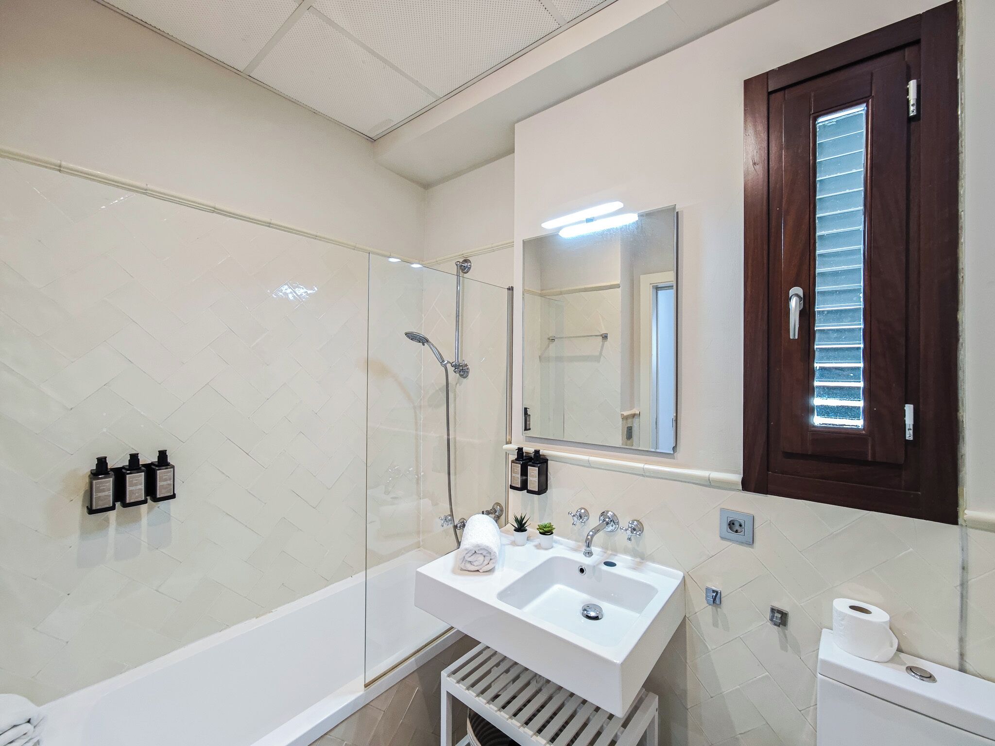 A modern bathroom with a glass-enclosed shower, a white sink with a mirror above it, and a wooden door with a window.