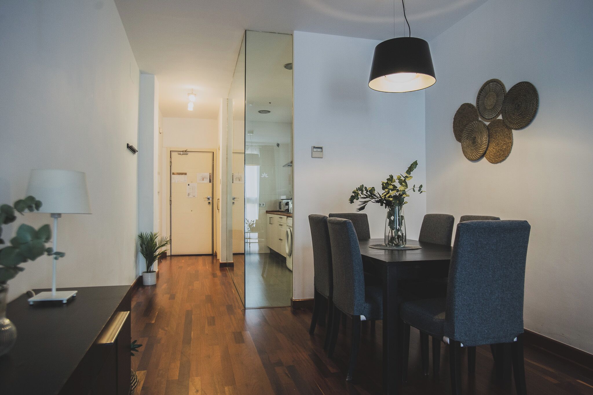 Un espace repas moderne avec un plancher en bois, une table à manger avec des chaises, un vase rempli de fleurs et un luminaire suspendu.