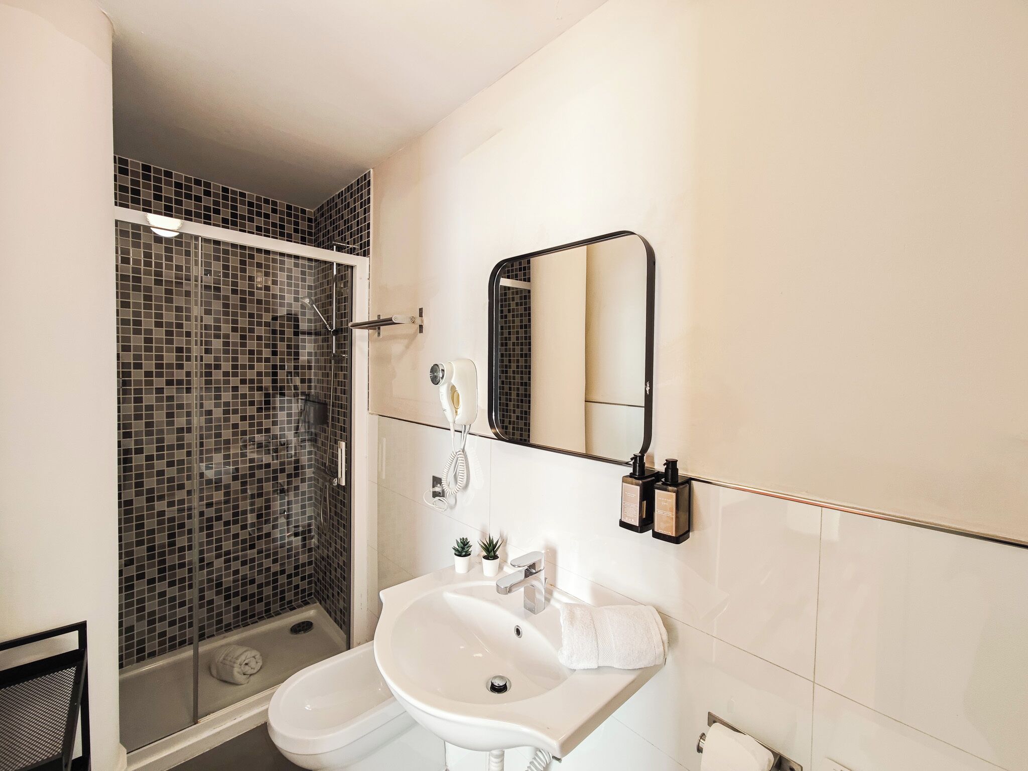 A bathroom with a shower, a sink, a mirror, and a towel rack.