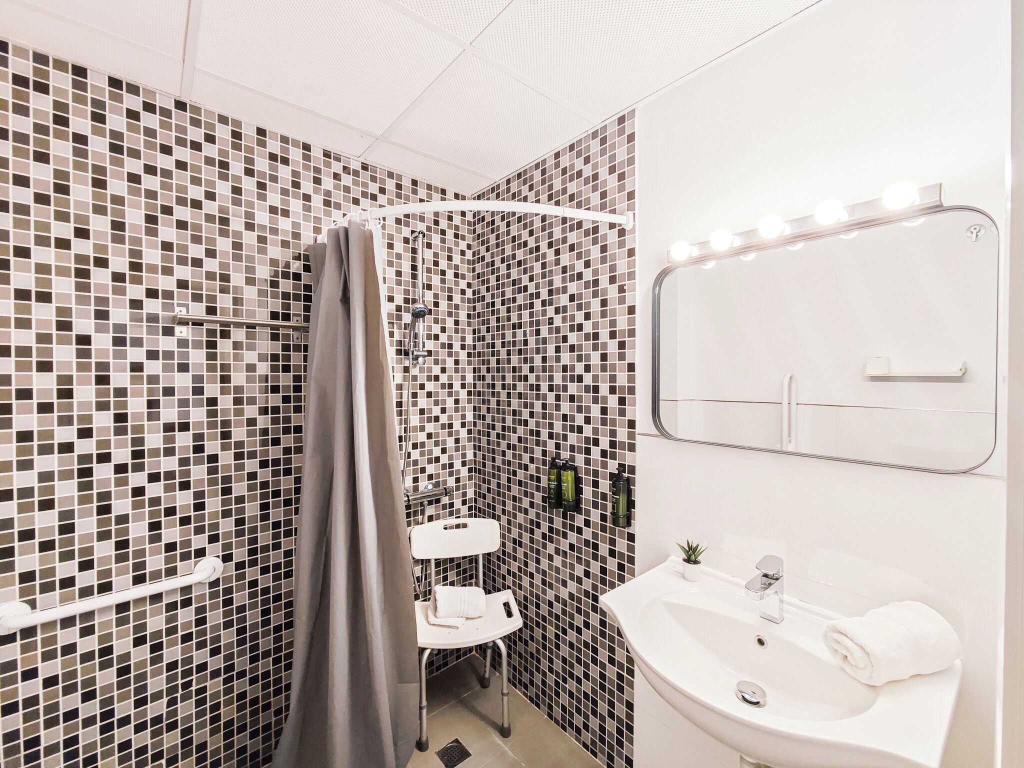 A bathroom with a shower, a sink, and a mirror with lights.