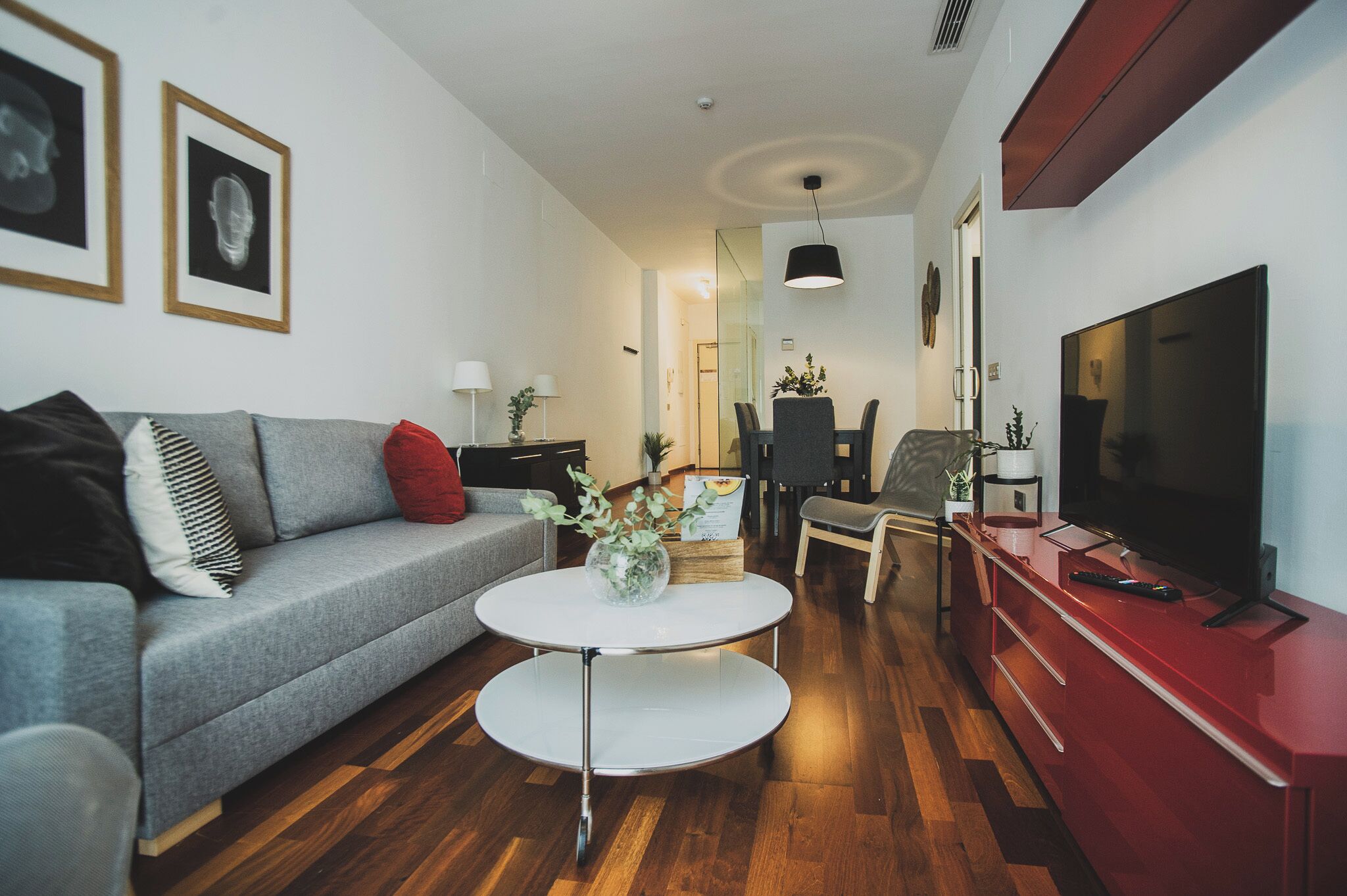 Un salon moderne avec un canapé gris, une table basse ronde, un meuble de rangement rouge et un téléviseur à écran plat.