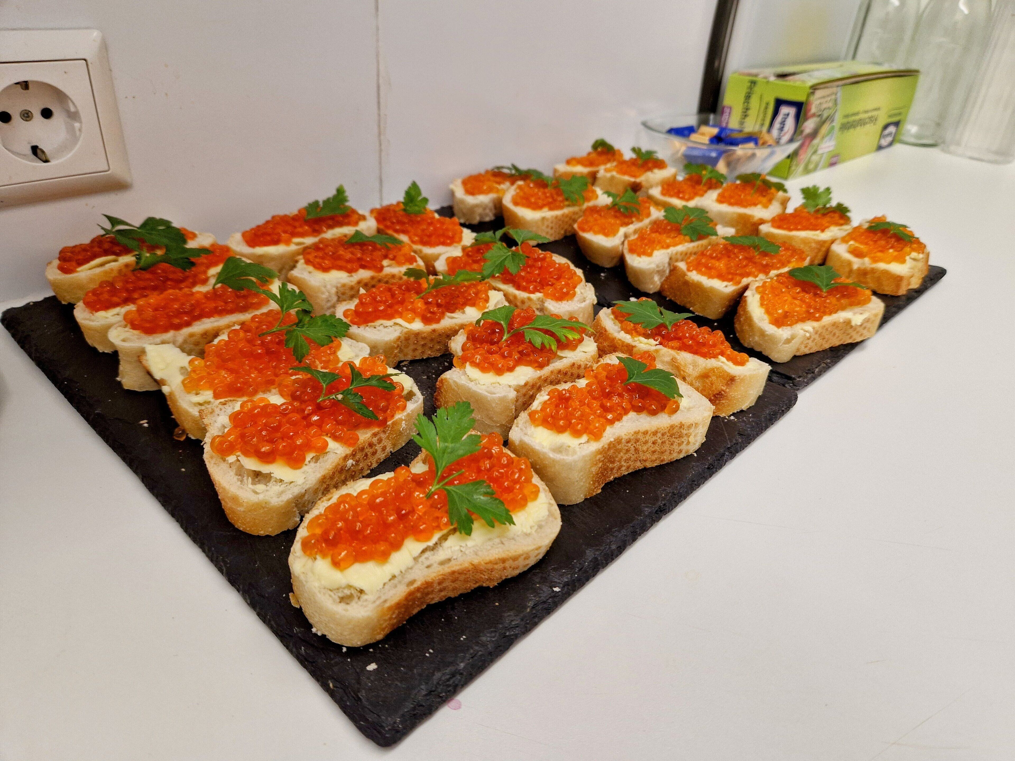 A black slate serving board with several pieces of toast topped with red caviar and parsley.