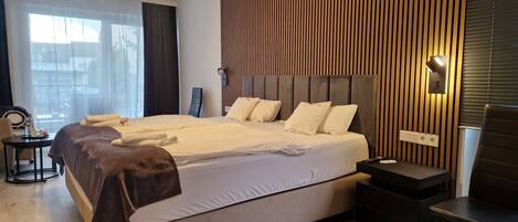 A modern hotel room with a large bed, bedside tables, and a view of the city through the window.