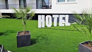 Et hotelskilt med ordet "HOTEL" i store hvide bogstaver på en grøn græsplæne, omgivet af plantekasser.