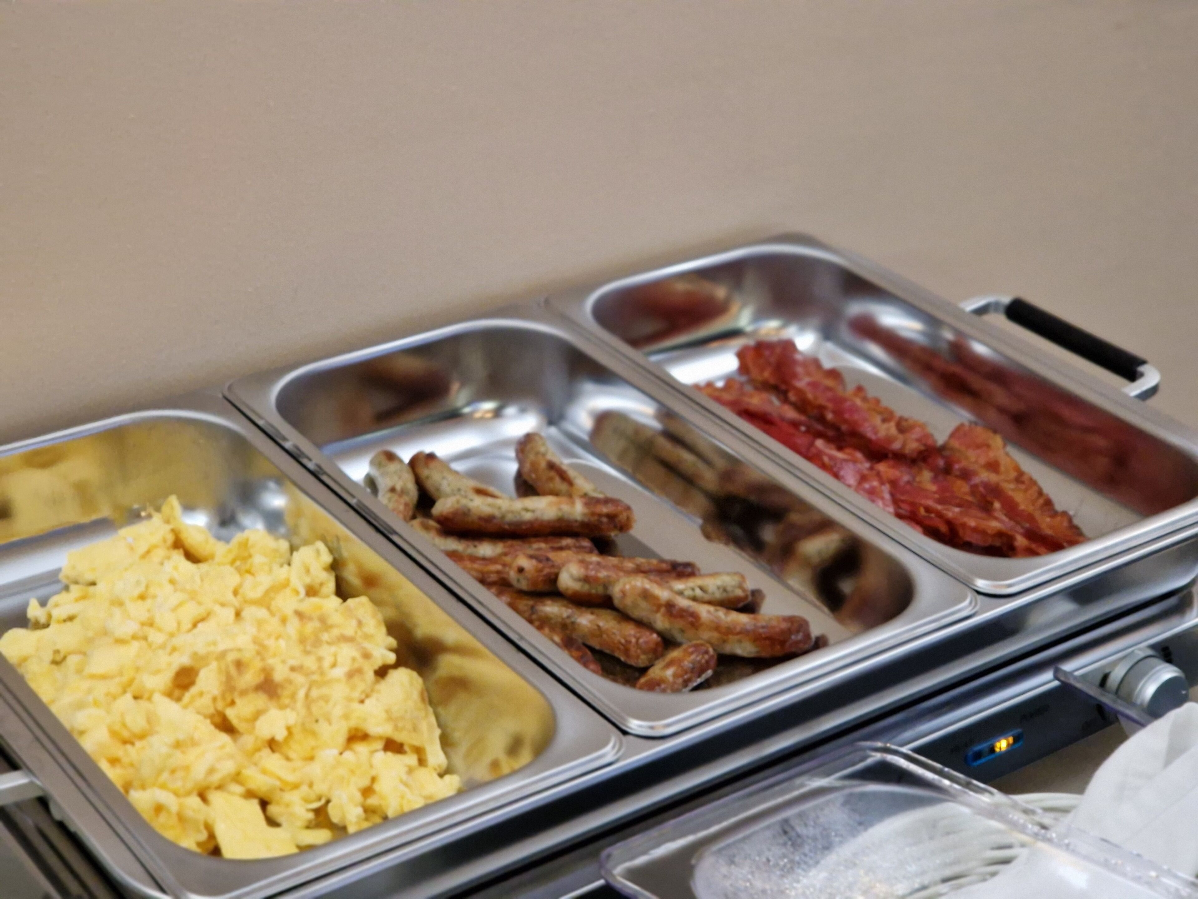 A buffet with scrambled eggs, sausages, and bacon.