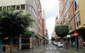 Eine schmale Stadtstraße, gesäumt von mehrstöckigen Gebäuden, von denen einige im Erdgeschoss Geschäfte beherbergen.