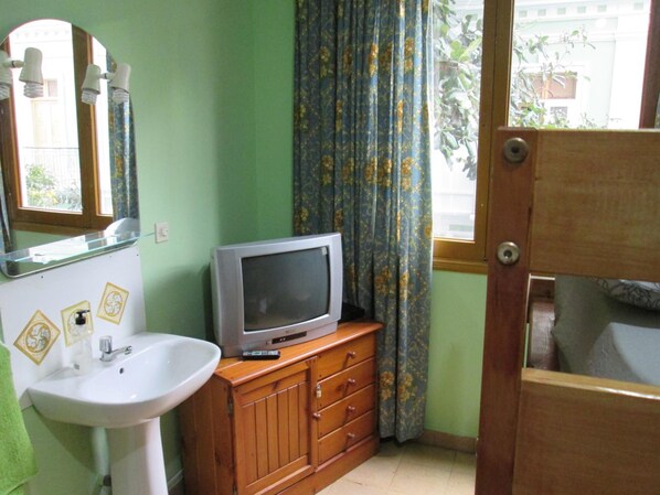 Un baño con lavamanos, espejo, armario de madera y un televisor encima.