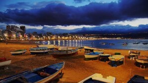 A beach with several boats lined up on the sand, a cityscape in the background, and a cloudy sky. - Pensión Sea of Clouds (Las Palmas de Gran Canaria)
