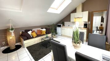 A modern loft-style apartment with a dining area, kitchenette, and a cozy seating area with a sofa and cushions.