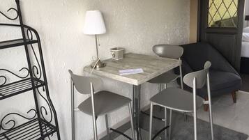 A small dining area with a table and four chairs, a metal shelf unit, a lamp, and a window with a view.