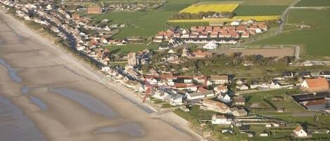 An aerial view of a coastal town with houses along the beach and fields in the background.