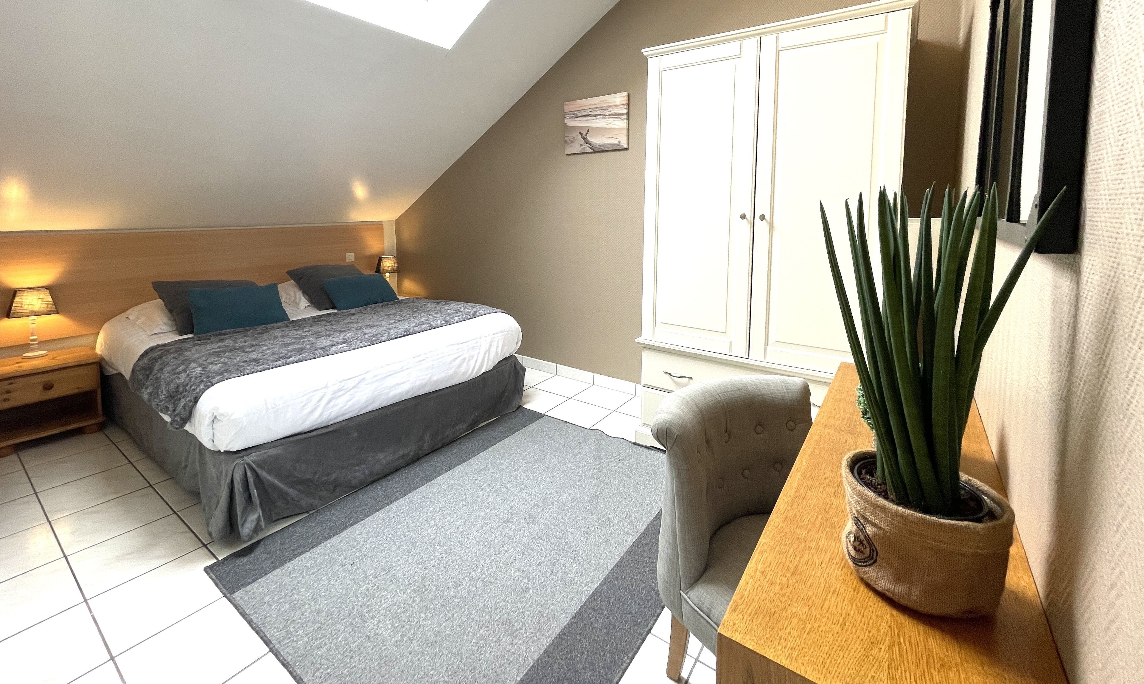 Une chambre à coucher comprenant un lit, une table de chevet, une lampe, une chaise, une armoire et une plante en pot.