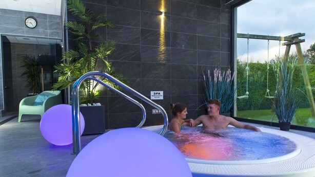 Een moderne, overdekte spa-ruimte met een bubbelbad, een klok en een bord dat een spa aangeeft.