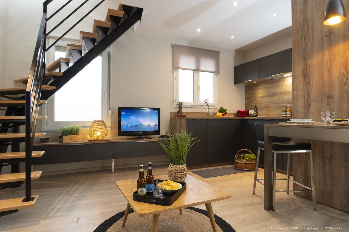 A modern kitchen with a wooden island, a dining area with a wooden table, and a staircase.