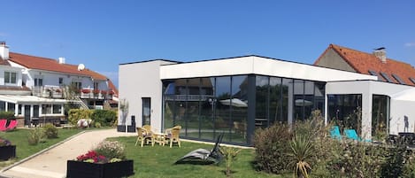 A modern building with large glass windows, a flat roof, and a well-maintained garden with outdoor seating.