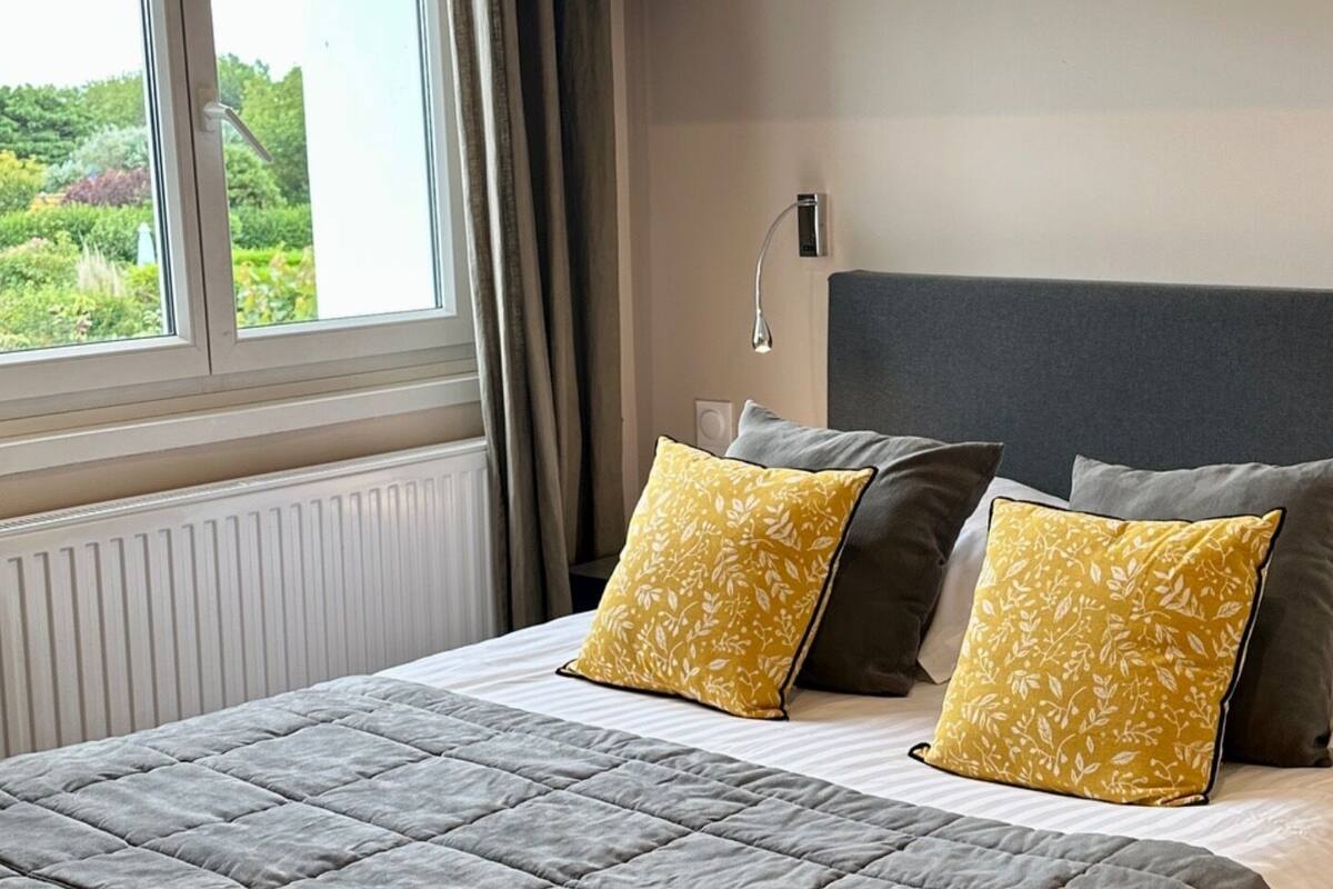 A neatly made bed with a grey quilt and two yellow pillows with a leaf pattern.