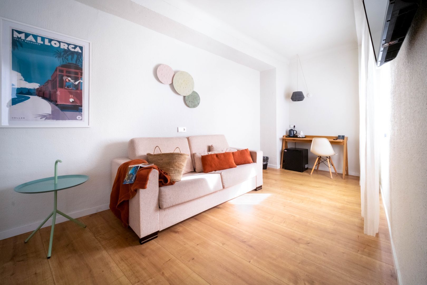 Una sala de estar con un sofá, una mesita, un cartel y un escritorio con una silla.
