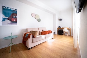 A living room with a sofa, a small table, a poster, and a desk with a chair. - Apuntadores 8 (Palma de Mallorca)