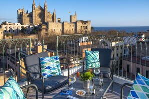 An outdoor balcony with two chairs, a table, and a view of a historic castle.