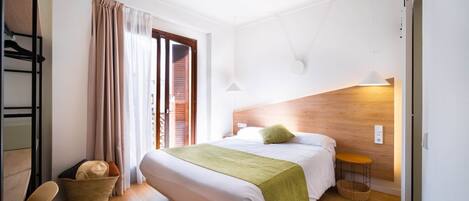 Una habitación de hotel con cama, una silla, una mesa, un cesto y una ventana con cortinas.
