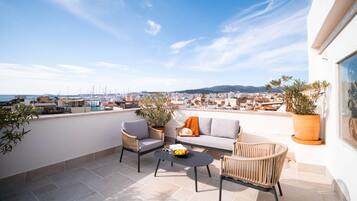 Una terraza en la azotea con mobiliario exterior, plantas en macetas y vistas al puerto deportivo y al paisaje urbano.