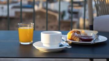 A table with a glass of orange juice, a cup, and a croissant on a balcony overlooking a coastal view.