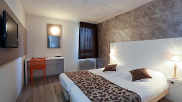 Habitación de hotel con cama, escritorio, silla y televisor montado en la pared.