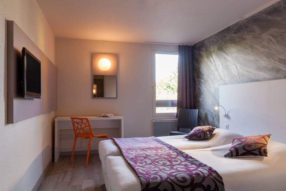 A hotel room with a bed, a desk, and a chair.