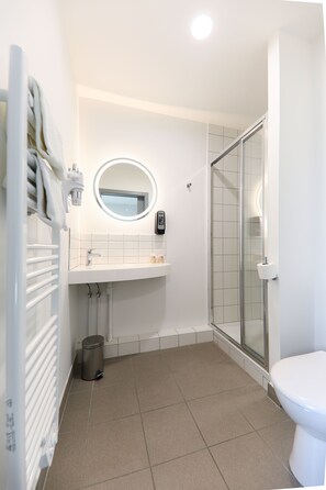 Features a sleek design with a round mirror, glass-enclosed shower, and toilet.