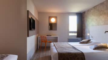 A hotel room with a bed, a desk, a chair, a television, and a window with curtains.