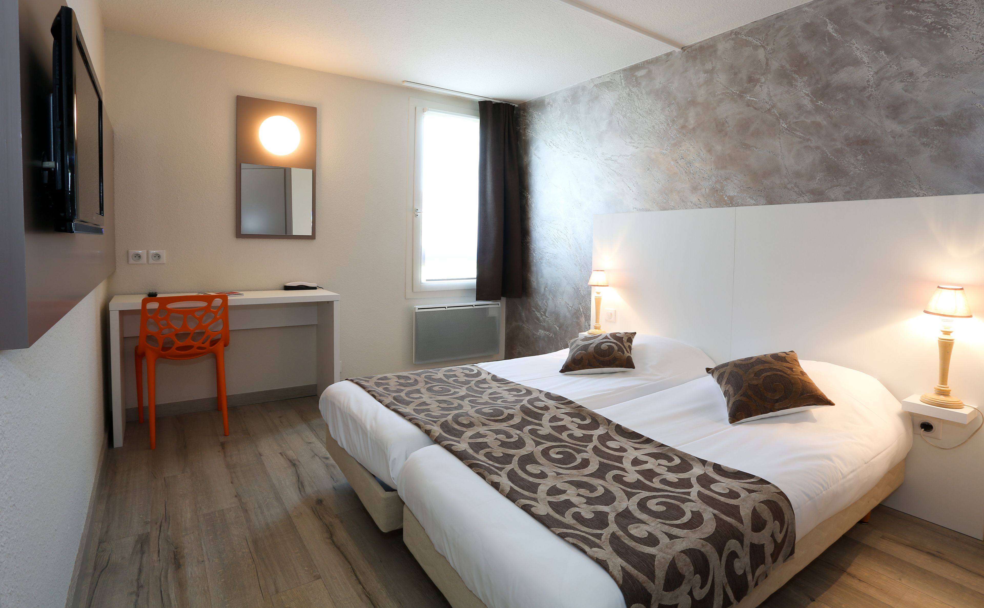 Una habitación de hotel con cama, escritorio, silla y dos lámparas de noche.