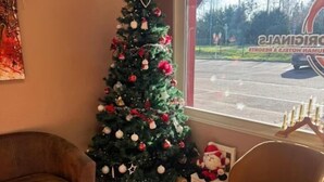 A cozy room with a Christmas tree, a brown leather sofa, a round glass table with a menu, and a window with a view of a parking lot. - The Originals City, Hotel Mulhouse, Ile Napoleon (Rixheim)