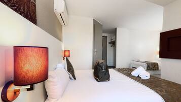 Een hotelkamer met een bed, een wandlamp, een koffer en een deur die naar een andere kamer leidt.