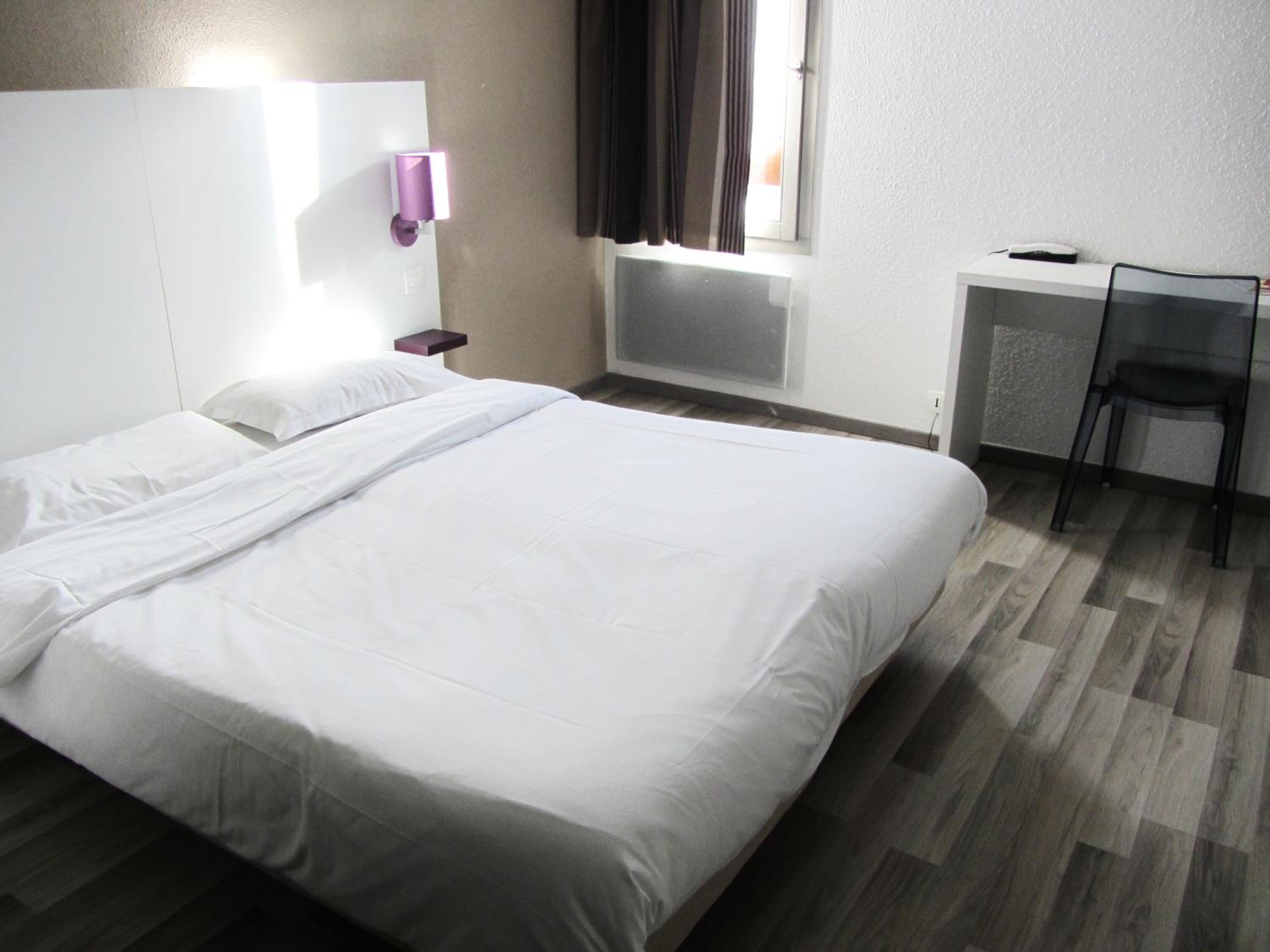 Een hotelkamer met een groot bed, een bureau, een stoel en een raam met gordijnen.