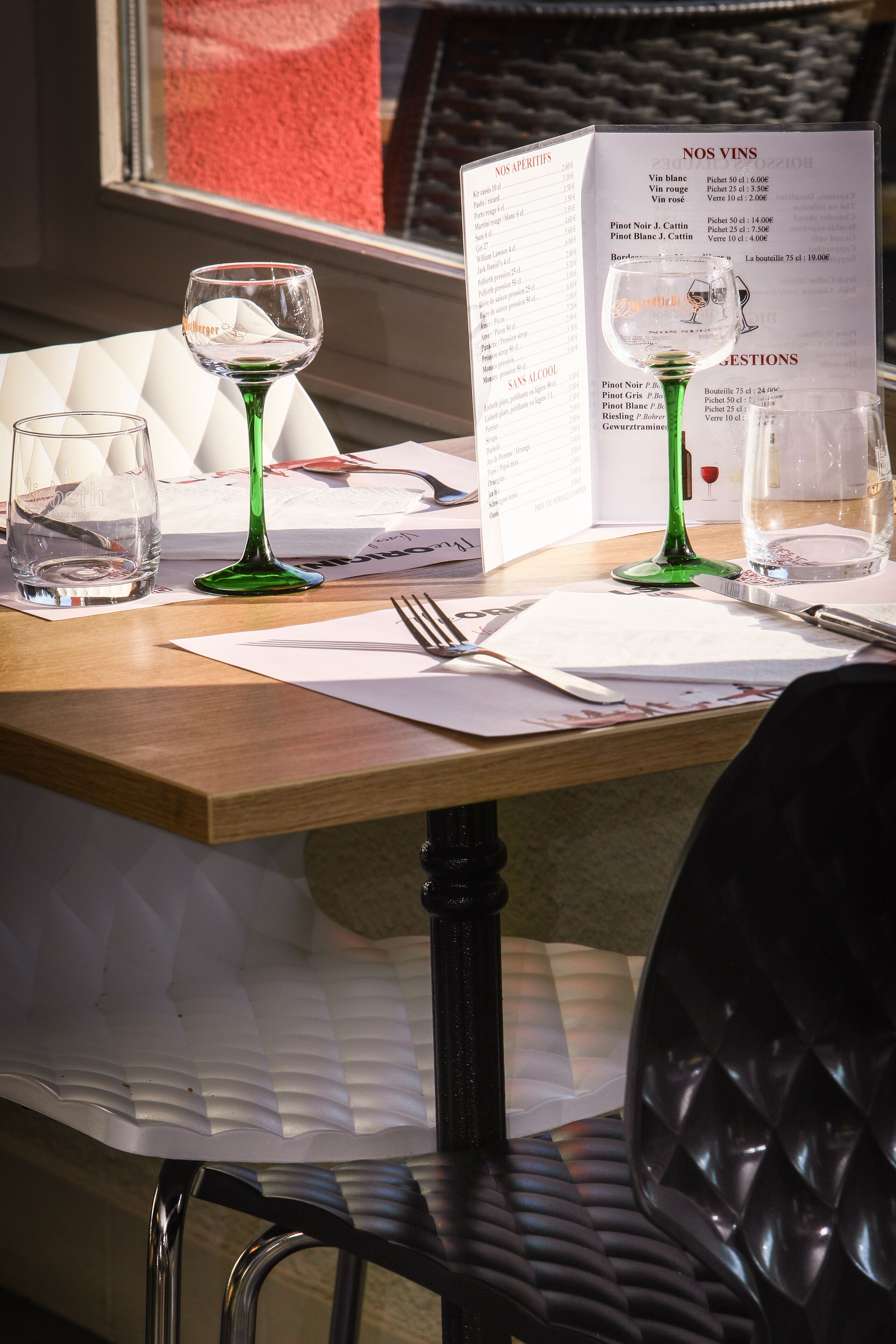 A table with a menu, two wine glasses, a water glass, and cutlery.